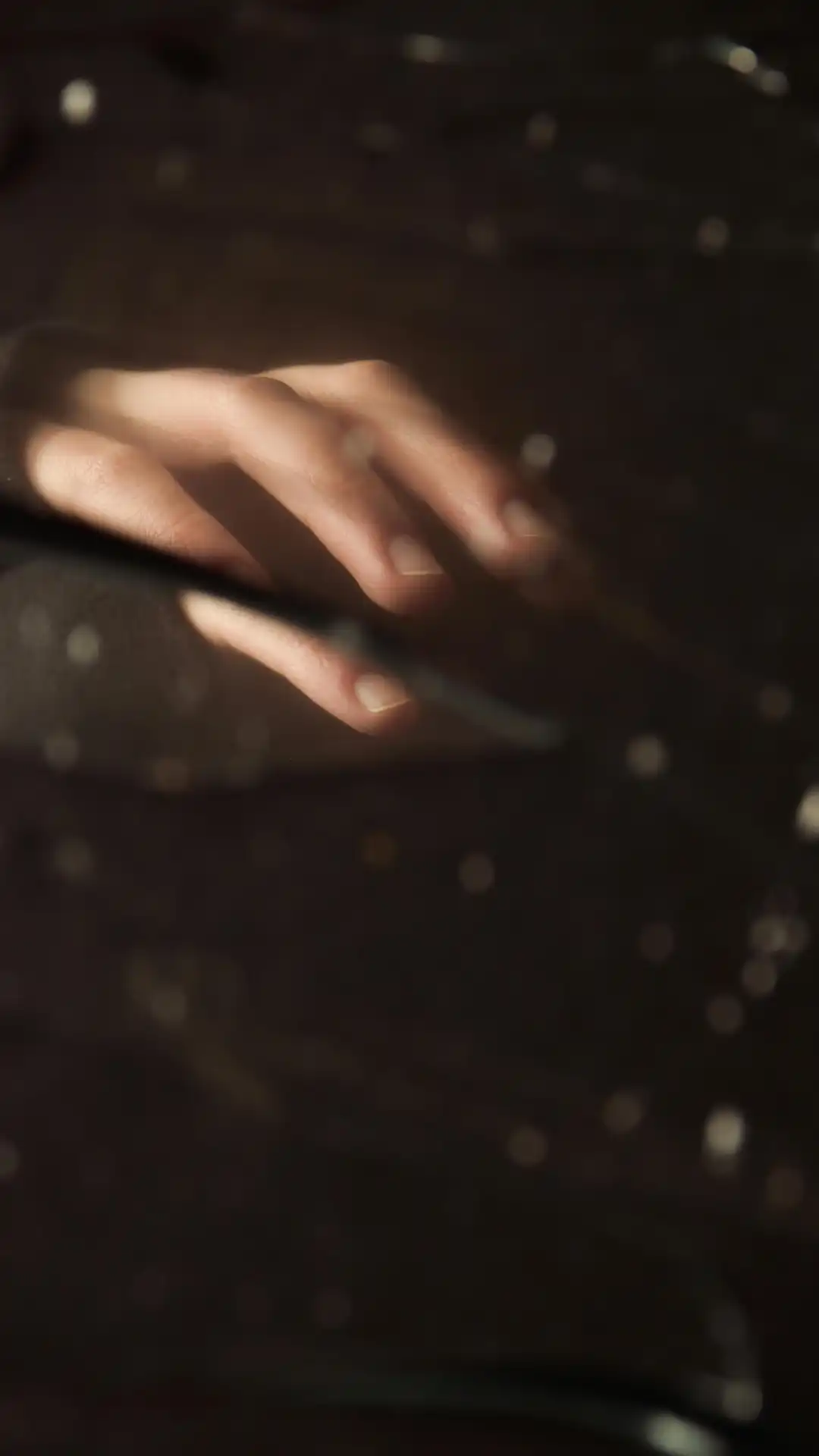 A hand reaching forward with soft bokeh light in a dark background