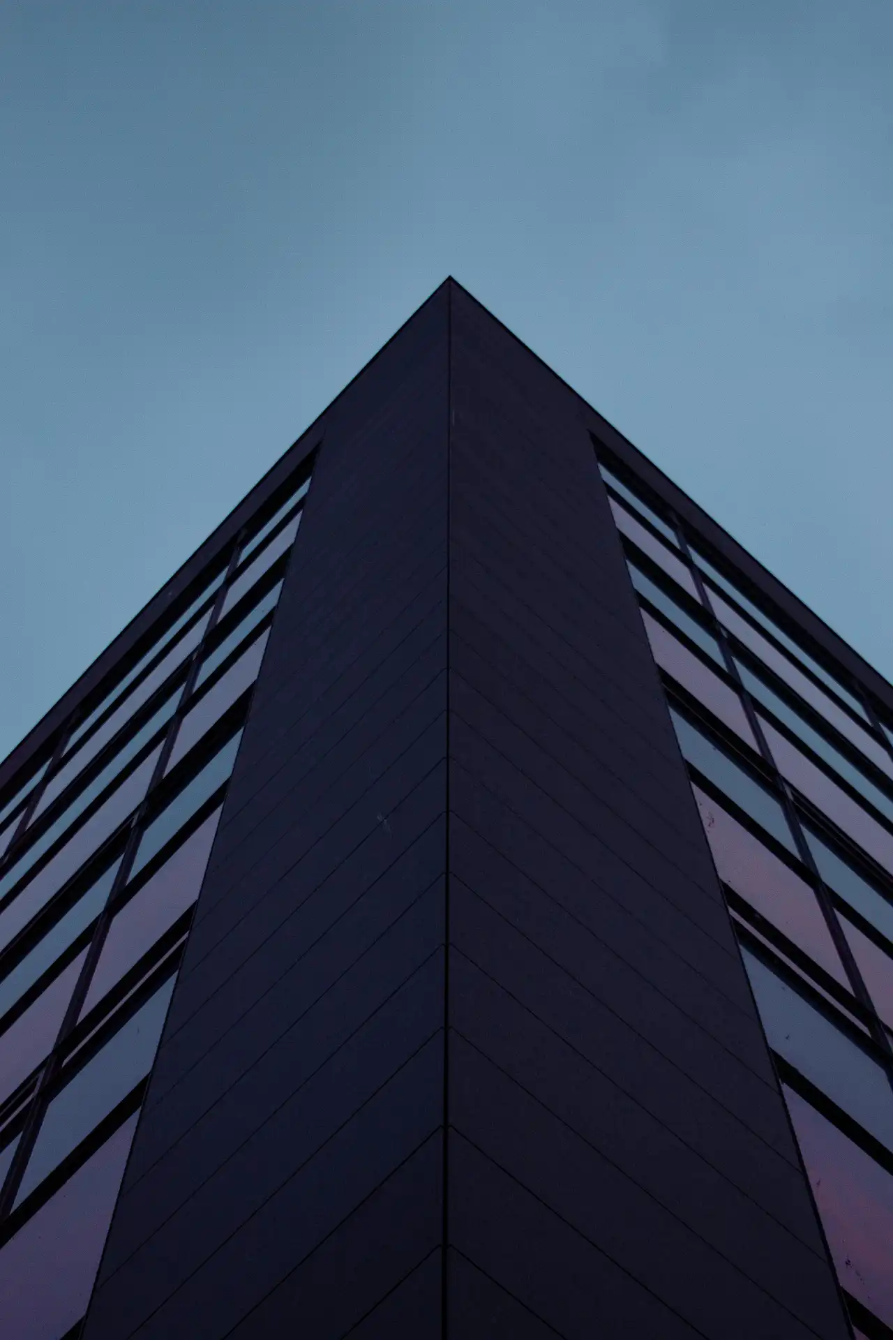 A sharp geometric building facade pointing upward against a purple night sky