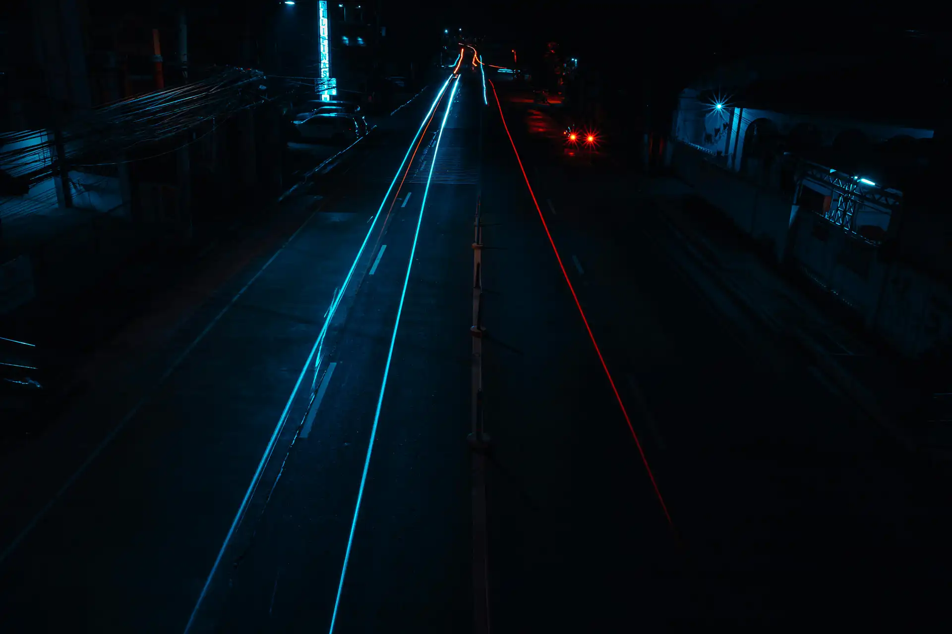 Teal and red light trails stretching down a dark empty road at night