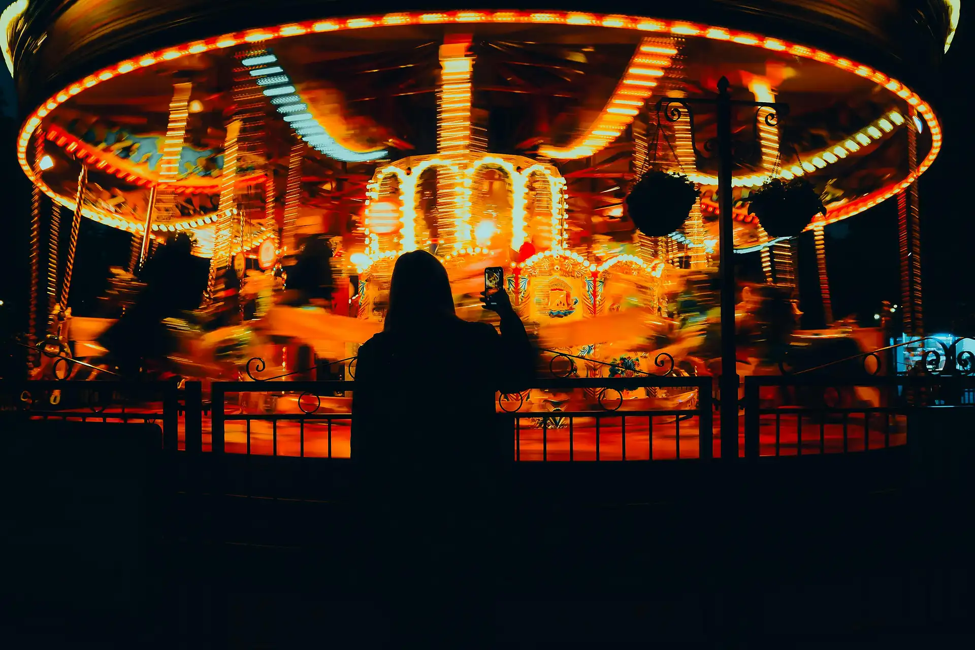 A silhouette of a person watching a spinning carousel illuminated the warm orange and red night at night